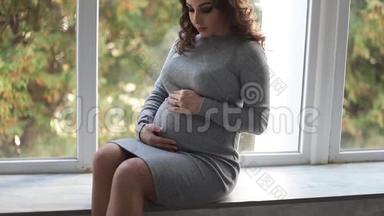 一位<strong>孕妇</strong>坐在家里靠窗的窗台上。她穿着漂亮的<strong>孕妇</strong>装
